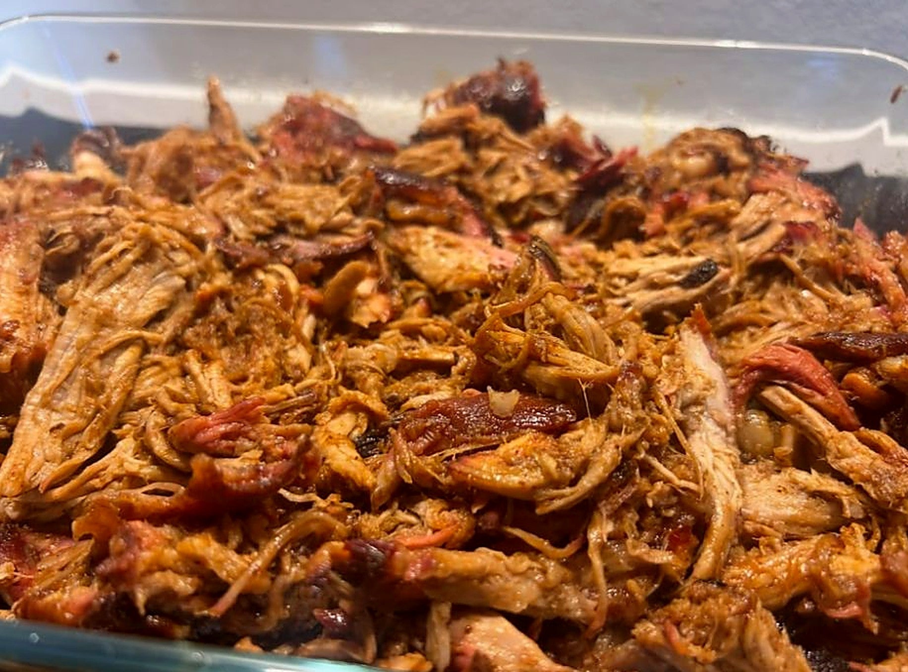 Pulled pork van de kamado met rokerige bark en smoke ring, getrokken in een glazen ovenschaal