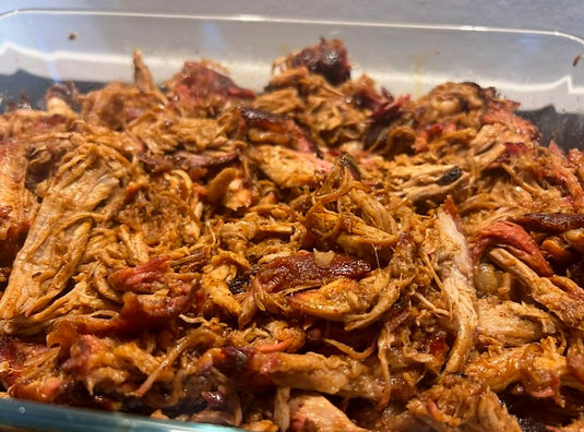 Pulled pork van de kamado met rokerige bark en smoke ring, getrokken in een glazen ovenschaal
